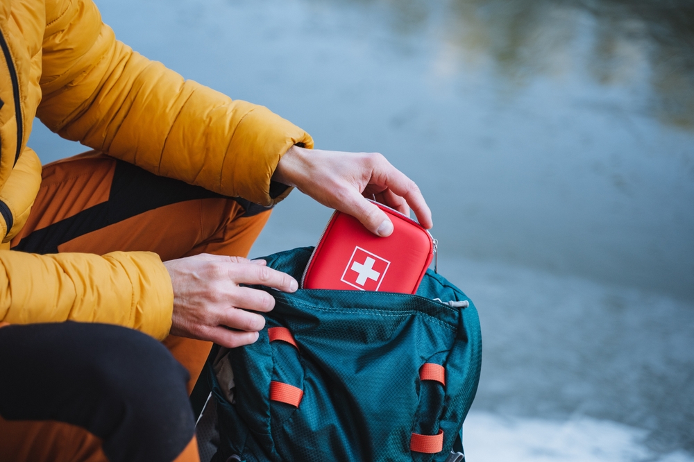Close-up of a person putting a red first aid kit into a green backpack.