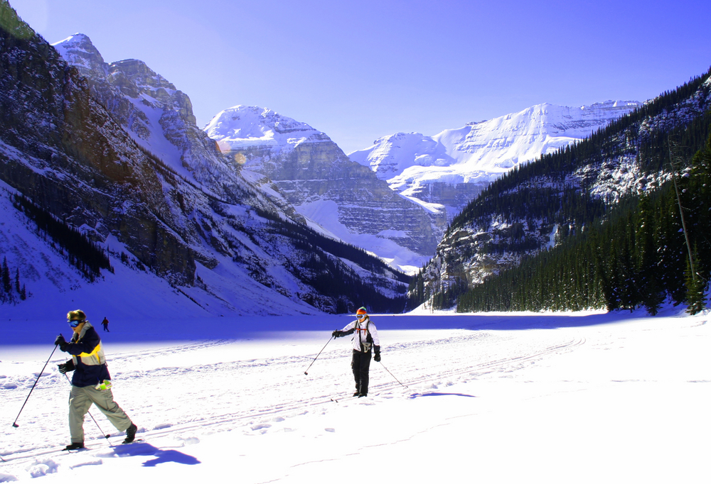 Two people cross-country skiing in a valley surrounded by mountains.