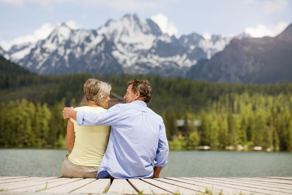 Retired couple sitting on a dock with mountains in the background.