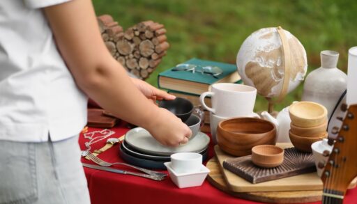 Close-up of a woman holding a pair of bowls with a table full of old items at a yard sale.