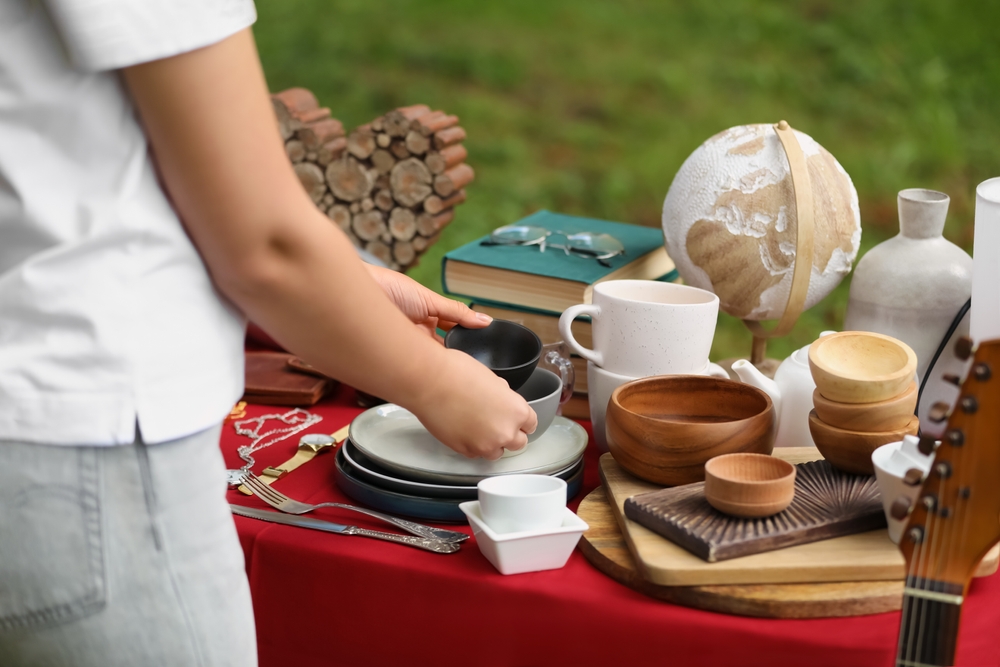Close-up of a woman holding a pair of bowls with a table full of old items at a yard sale.