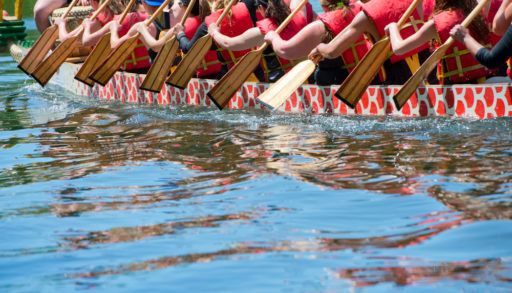 Close-up of paddles above the water as people paddle a dragon boat.