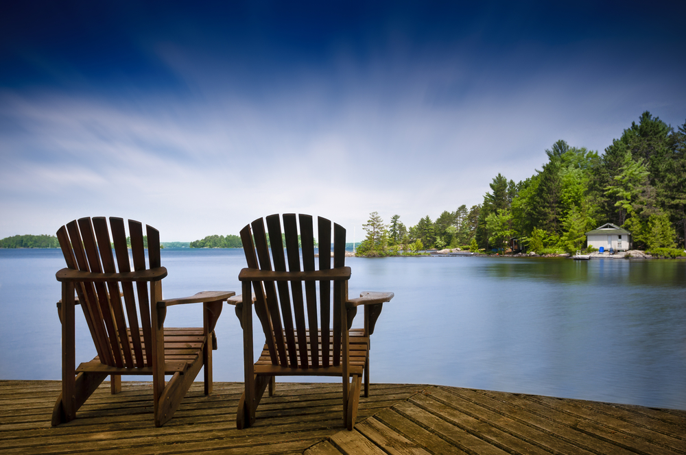 Two Muskoka chairs on a dock overlooking a lake.