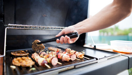 Close-up of a man's hand using tongs to flip steak on a grill.