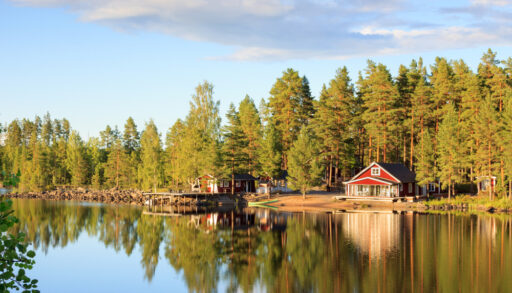 Traditional red cottage on a lake surrounded by trees.