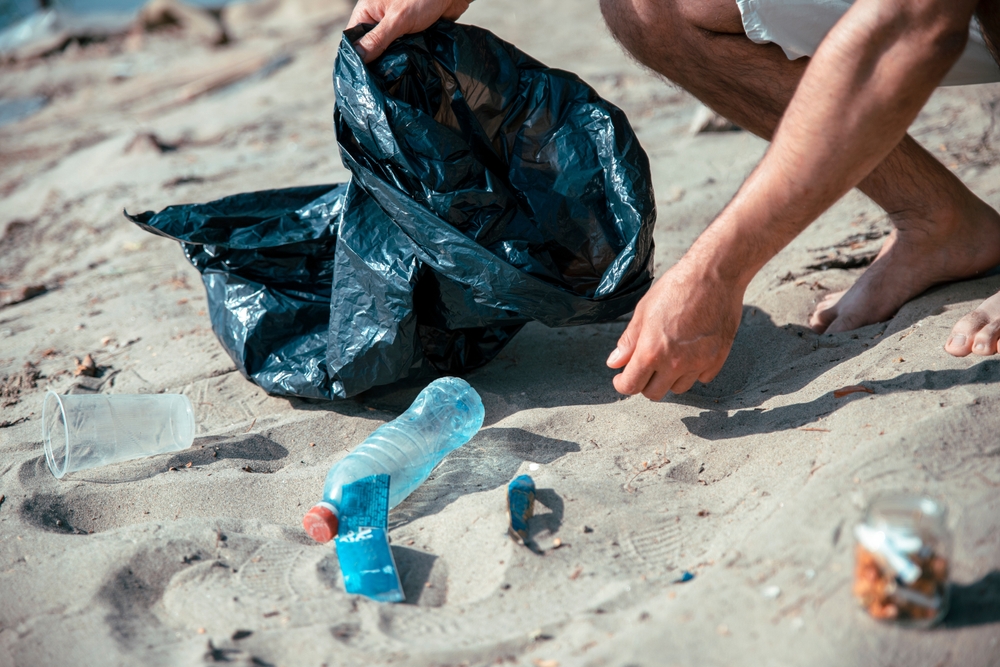 Close-up of a person picking up trash on a beach.
