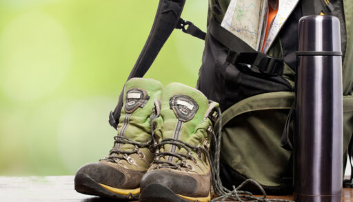Close-up of outdoor equipment like hiking boots, a backpack and a water bottle.
