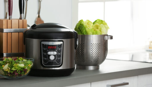 Modern slow cooker on a kitchen counter next to bowls of vegetables.