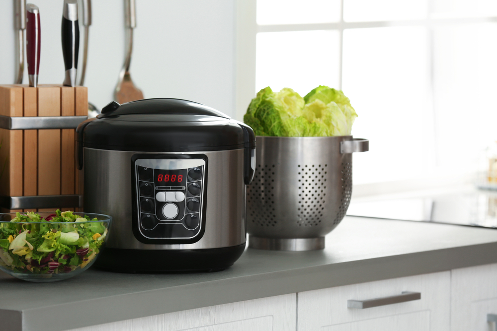 Modern slow cooker on a kitchen counter next to bowls of vegetables.