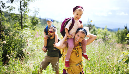 Family hiking in a field, with a woman carrying a kid on her shoulders.
