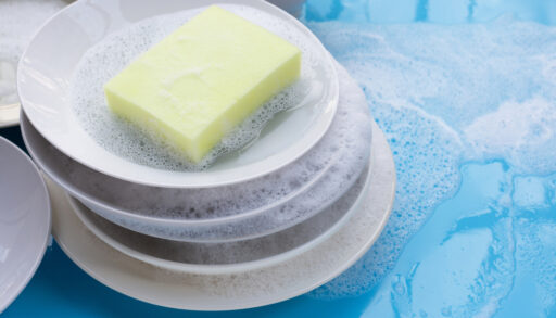 Stack of soap-covered dishes with a yellow sponge sitting on top.