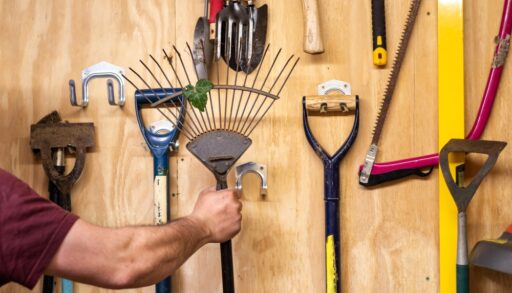 Close-up of a man taking a garden rake off a tool rack.