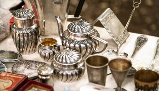 Antique silver teapots on a table with other antiques.