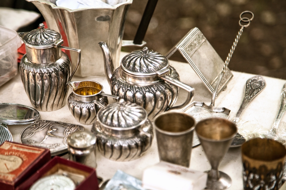 Antique silver teapots on a table with other antiques.