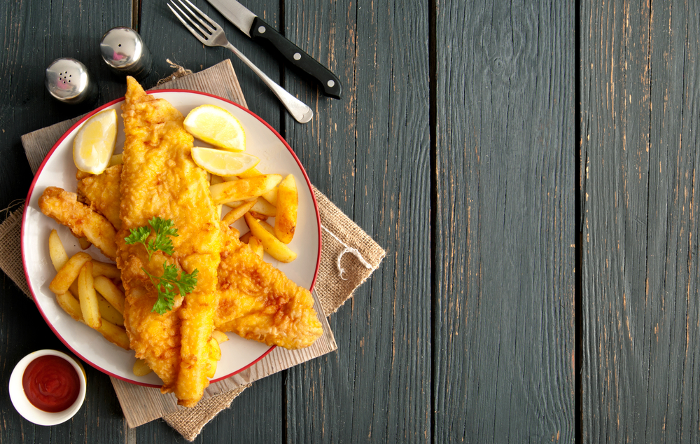 Overhead view of a plate of fish and chips next to a fork and knife.