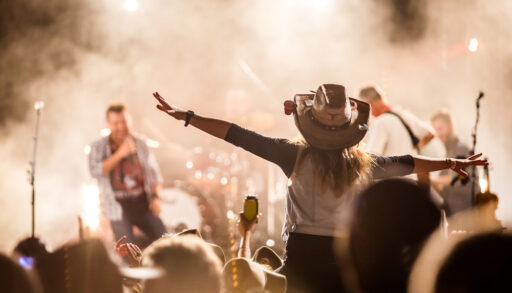 Crowd at a music festival with a young woman wearing a cowboy hat near the stage.