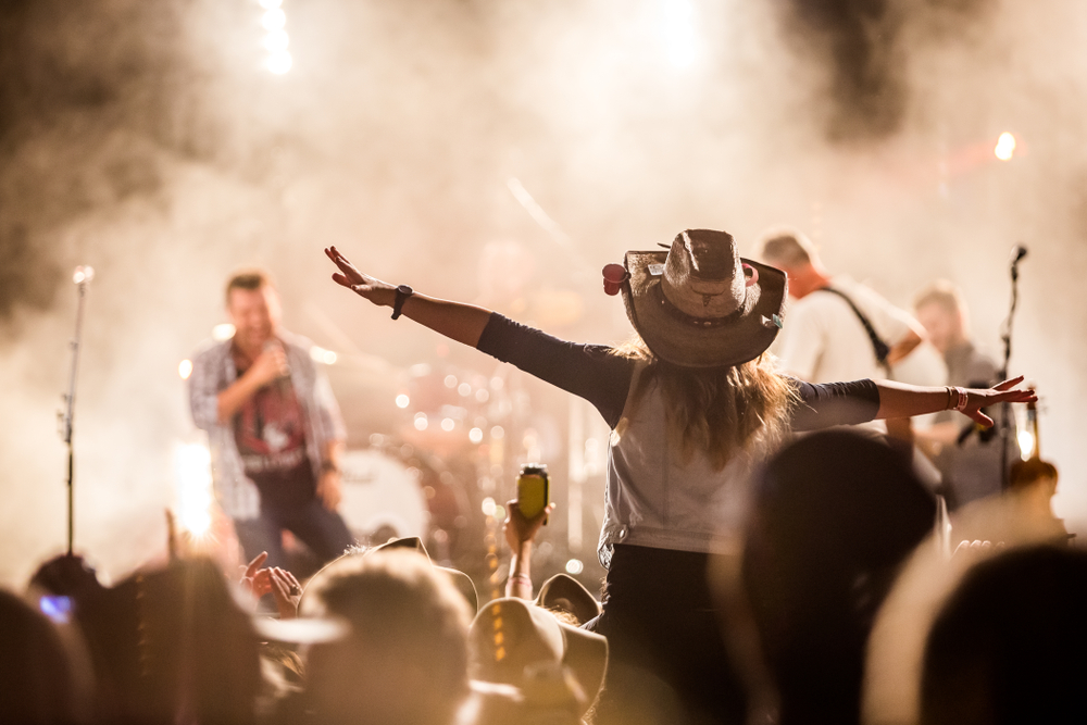 Crowd at a music festival with a young woman wearing a cowboy hat near the stage.