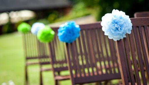 Blue and green paper flowers on wooden chairs at a wedding ceremony.