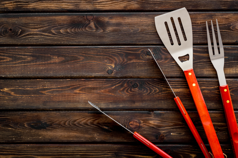 A red spatula, grill fork and tongs on a wooden background.