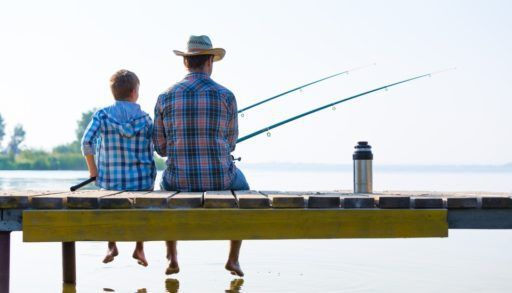 Father and son sitting on a wooden dock fishing.