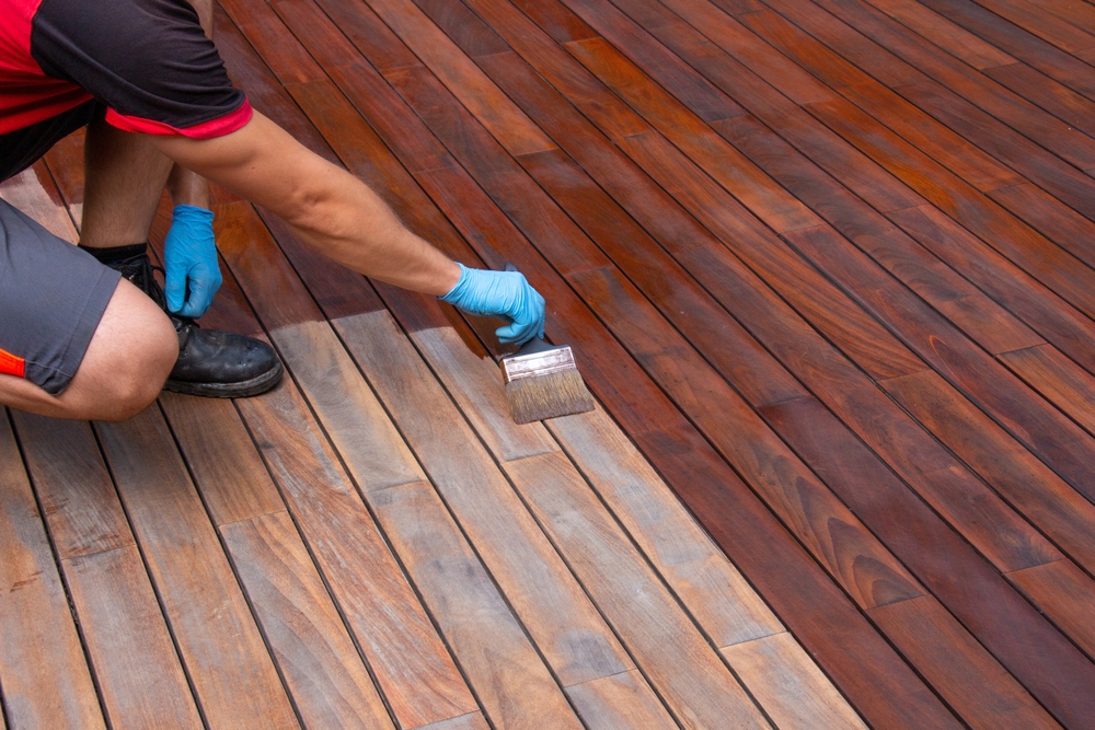 Close-up of a person applying a dark stain to a deck.