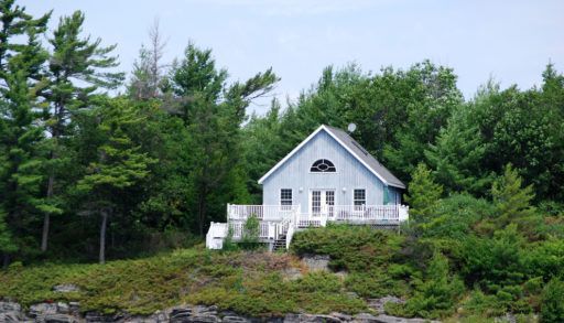 Cottage on a rocky shore surrounded by trees.