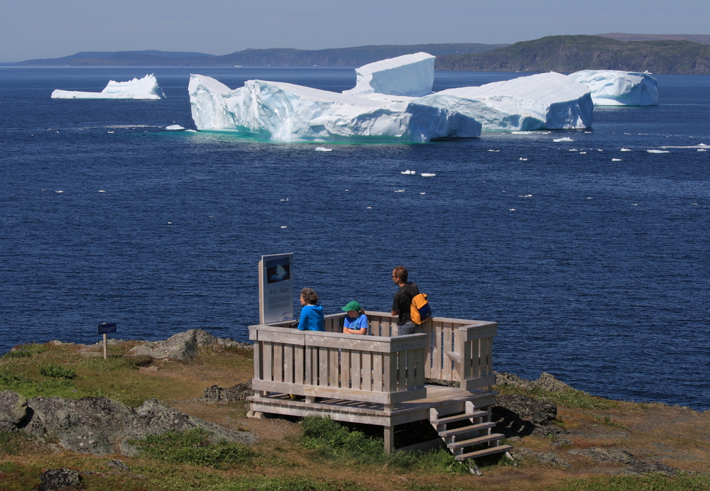 Tourists standing on a wooden platform watching icebergs in Iceberg Alley, Goose Cove, Newfoundland.