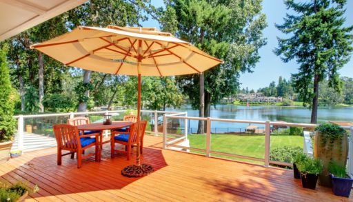 Patio table with an umbrella and chairs on a deck overlooking a lake.