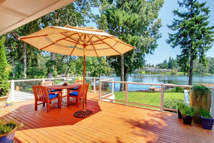 Patio table with an umbrella and chairs on a deck overlooking a lake.