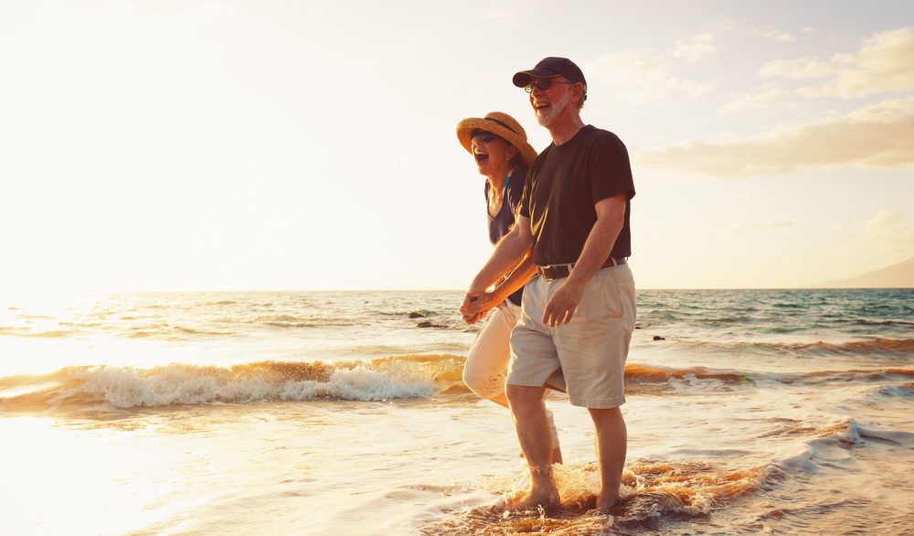 Smiling older couple walking hand-in-hand along a beach at sunset.