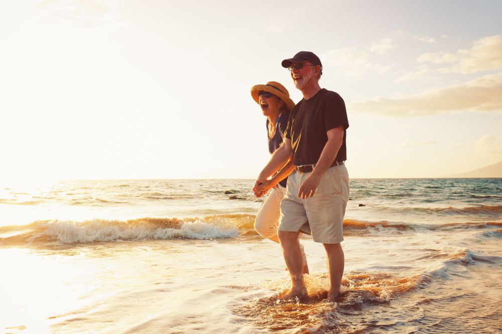 Smiling older couple walking hand-in-hand along a beach at sunset.