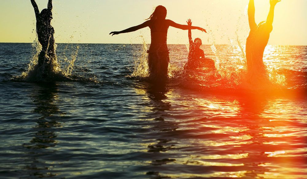 Silhouette of a group of friends jumping in an ocean at sunset.
