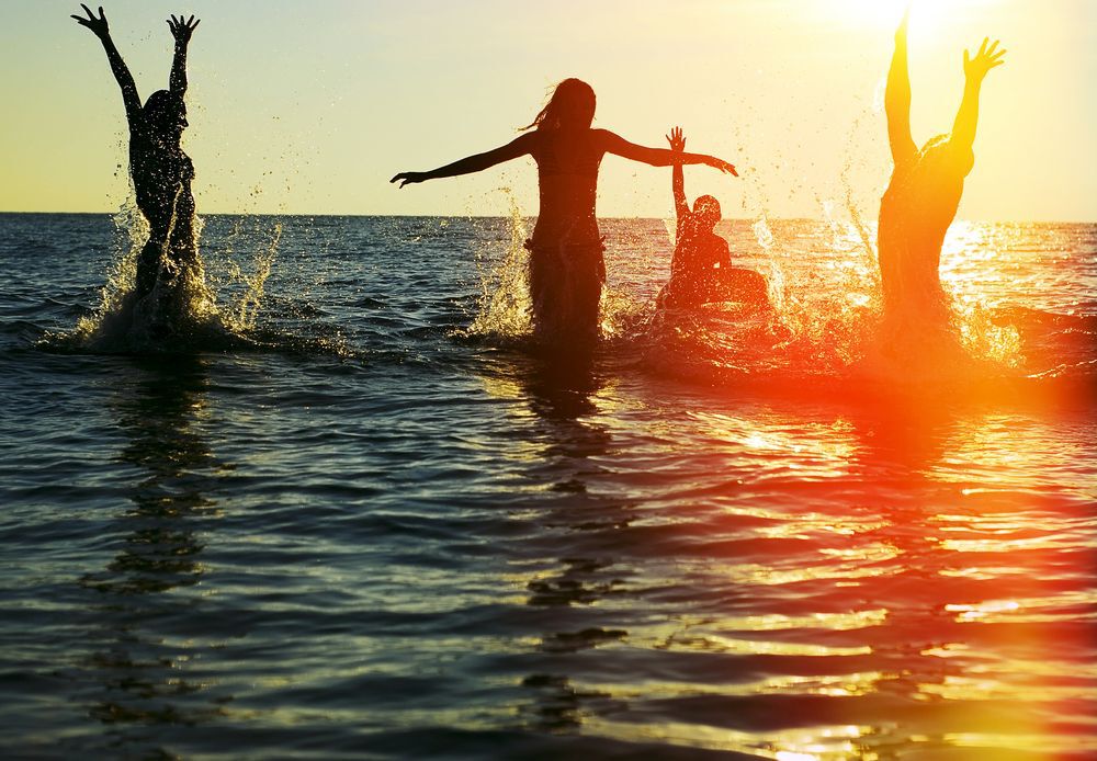 Silhouette of a group of friends jumping in an ocean at sunset.