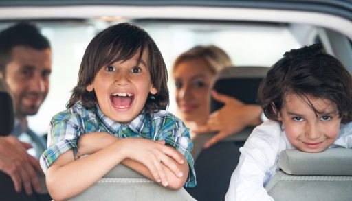 Two smiling kids looking out the backseat of a car.