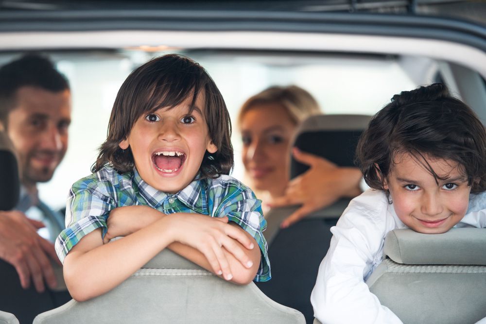 Two smiling kids looking out the backseat of a car.