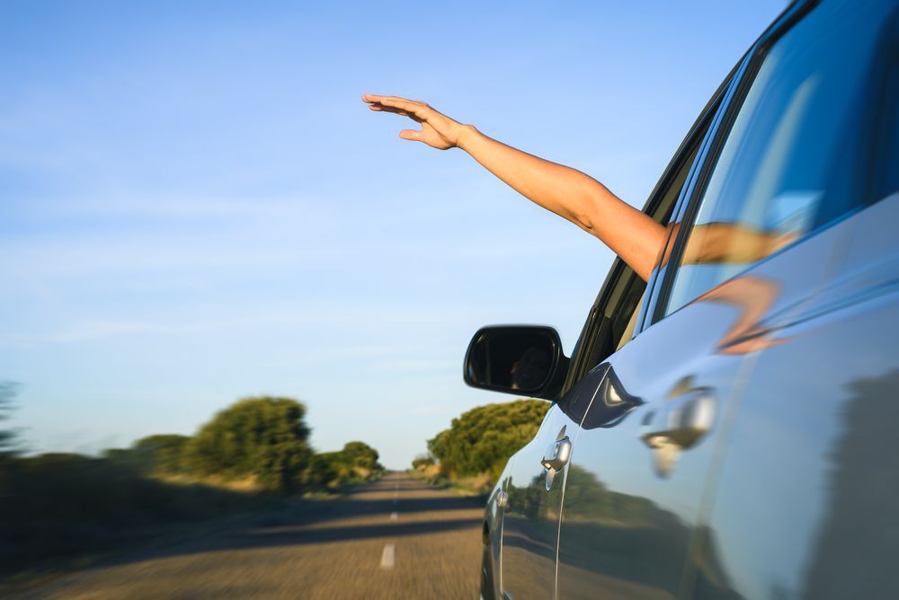 Person with their hand out a car window while driving.