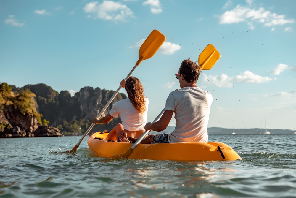 Young couple paddling on a lake in a yellow kayak.