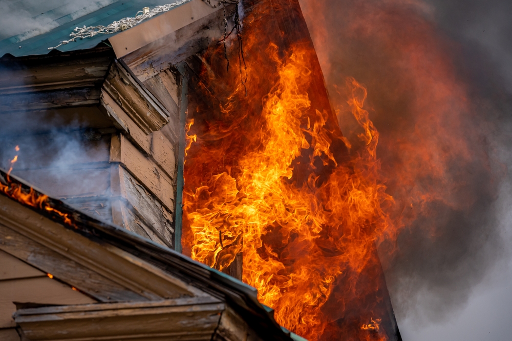 Two-storey wooden cottage with flames and smoke coming out a window.