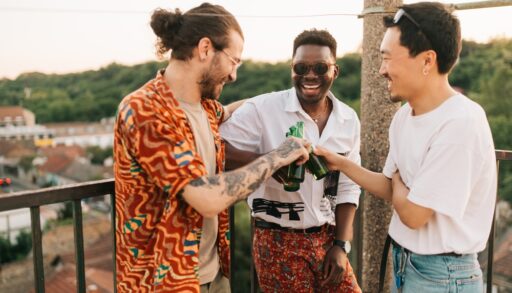 Three men toasting at a bachelor party on a rooftop balcony.