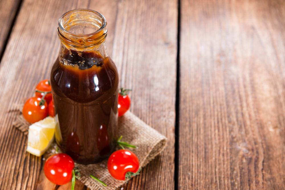 A bottle of barbecue sauce on a table next to small, red tomatoes.