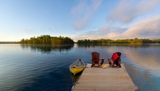 Two Adirondack chairs on a dock next to a yellow canoe.