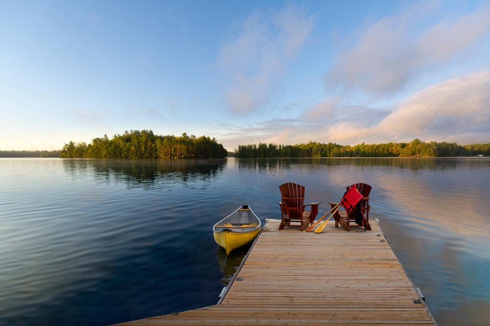Two Adirondack chairs on a dock next to a yellow canoe.