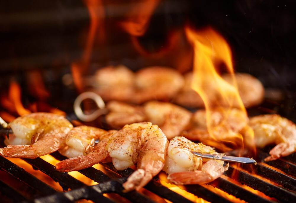 Close-up of shrimp on metal skewers cooking on a barbecue.
