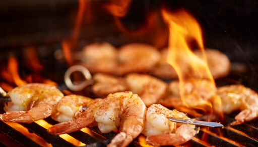 Close-up of shrimp on metal skewers cooking on a barbecue.