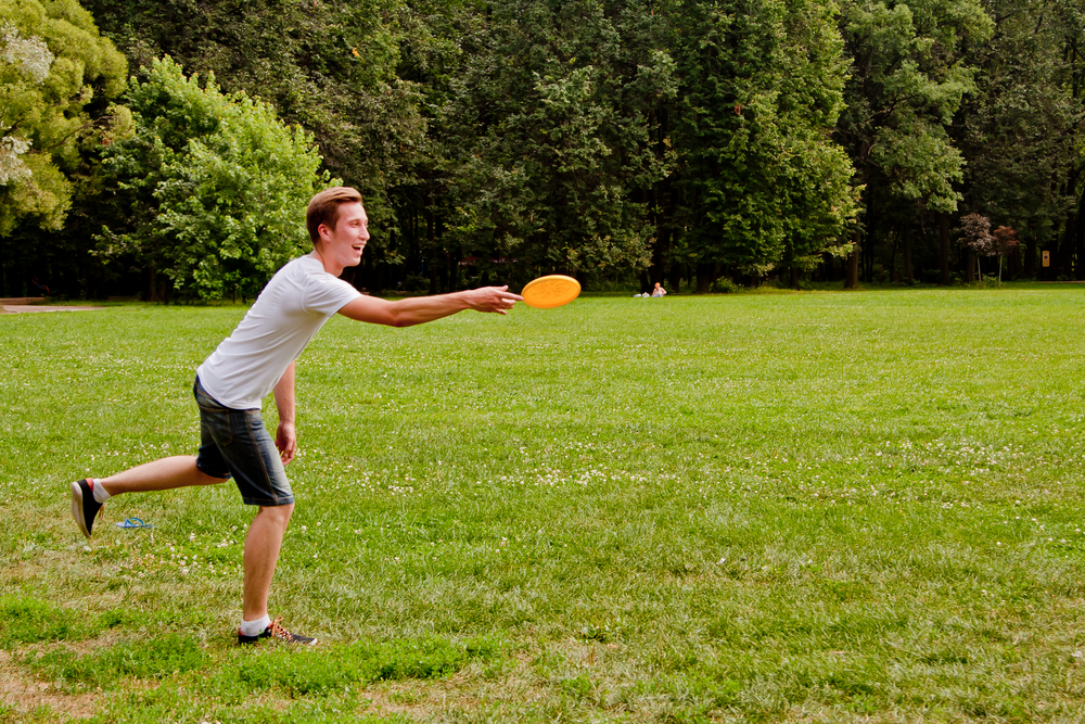 Young man throwing an orange frisbee in a green field.