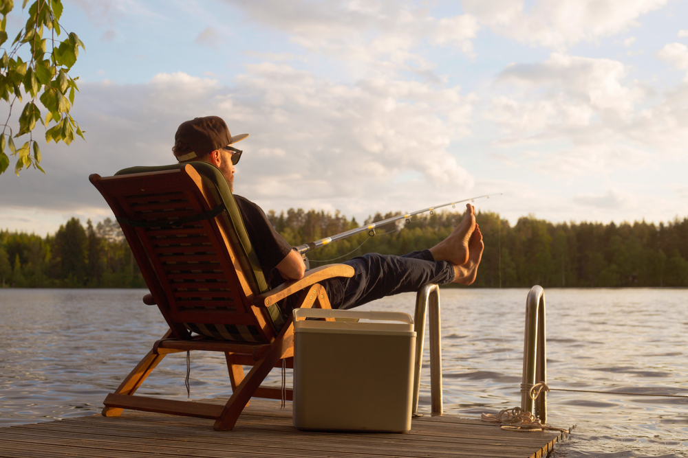 Man with his feet up, sitting on a dock and fishing.