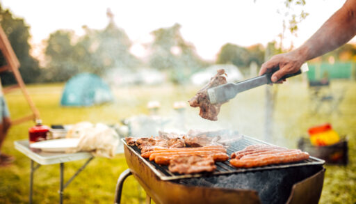 Close-up of a person flipping food on a barbecue in a park.