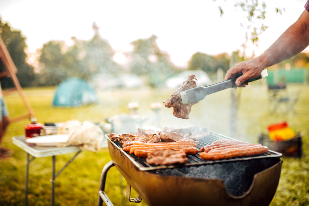 Close-up of a person flipping food on a barbecue in a park.