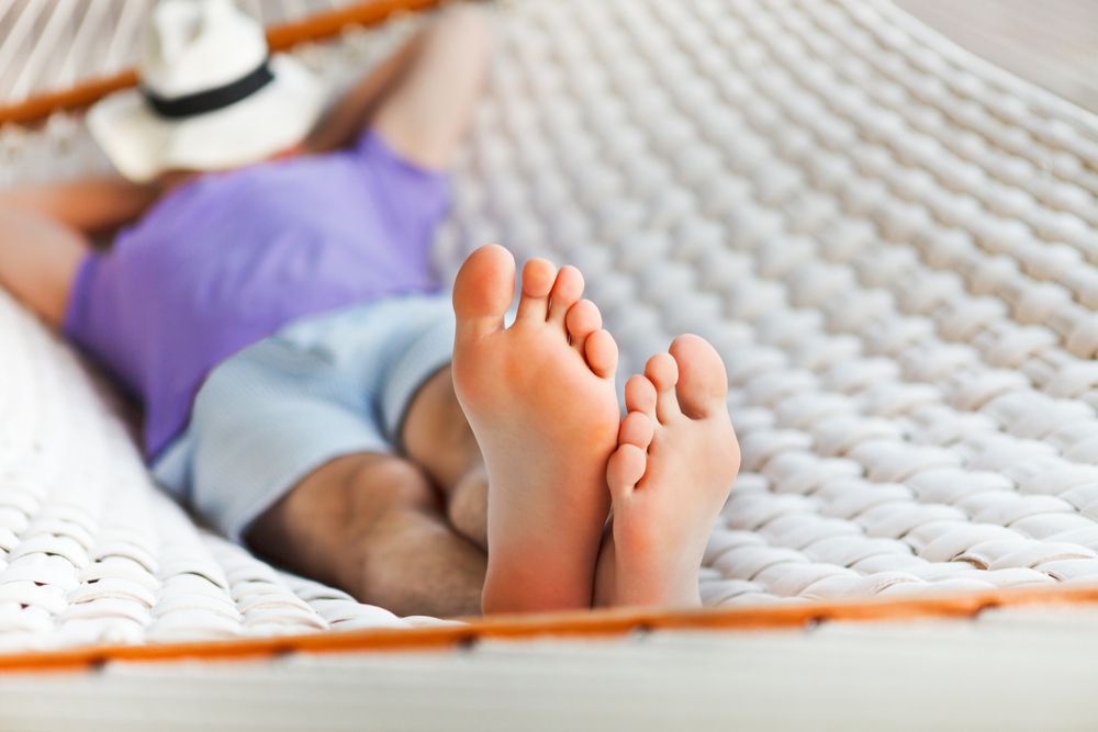 Close-up of a man's feet as he lays on a hammock, napping.