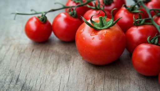 Close-up to red tomatoes attached to a green vine on a wooden table.